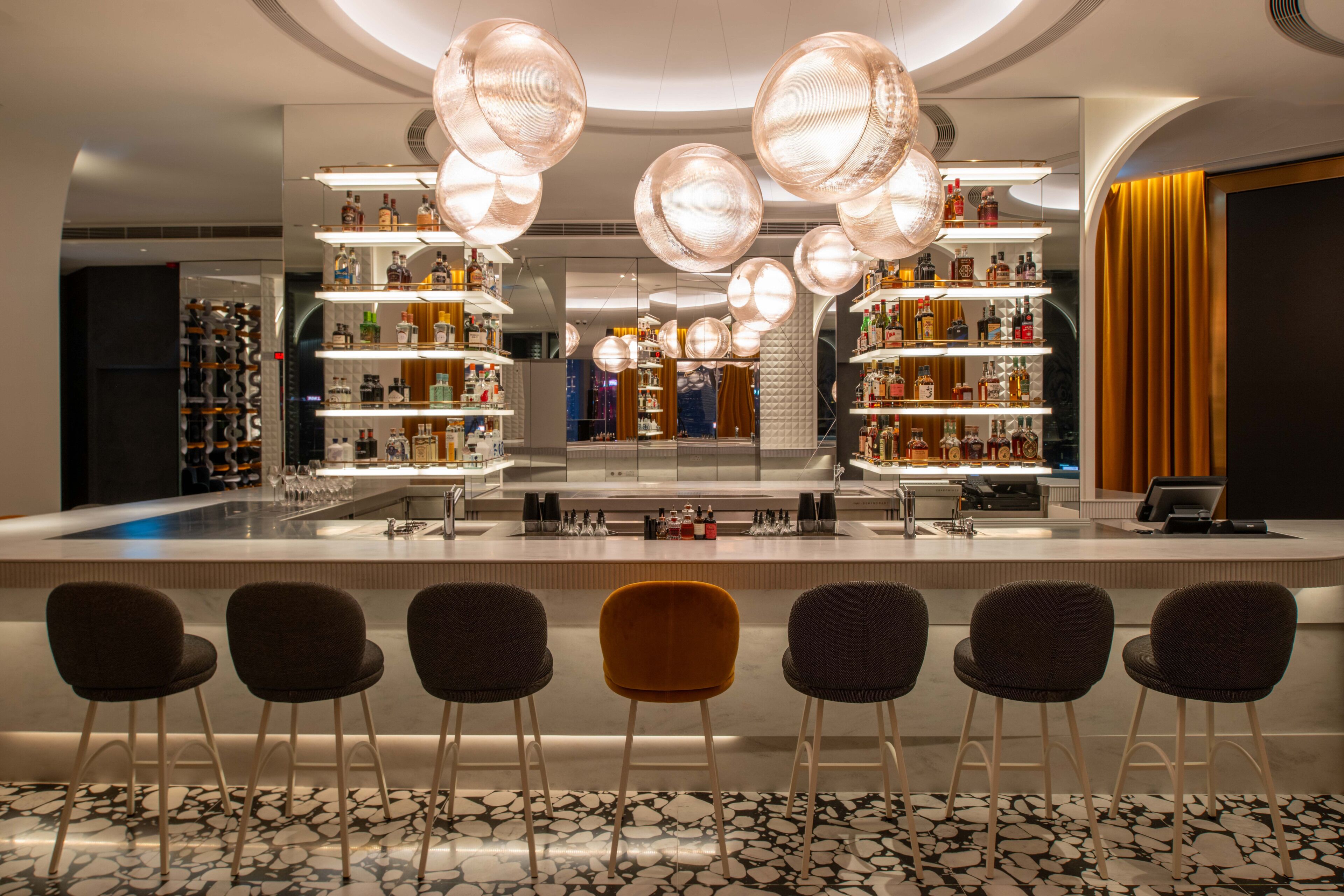 A bar area with a central island, bar stools, and shelves stocked with bottles.