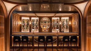 A bar area with a bar counter, two bar stools, and shelves of liquor bottles. - Mondrian Hong Kong (Kowloon)