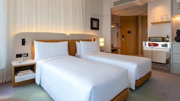 A hotel room with two beds, a bedside table with a lamp, a wardrobe, and a small seating area with a table and chairs.
