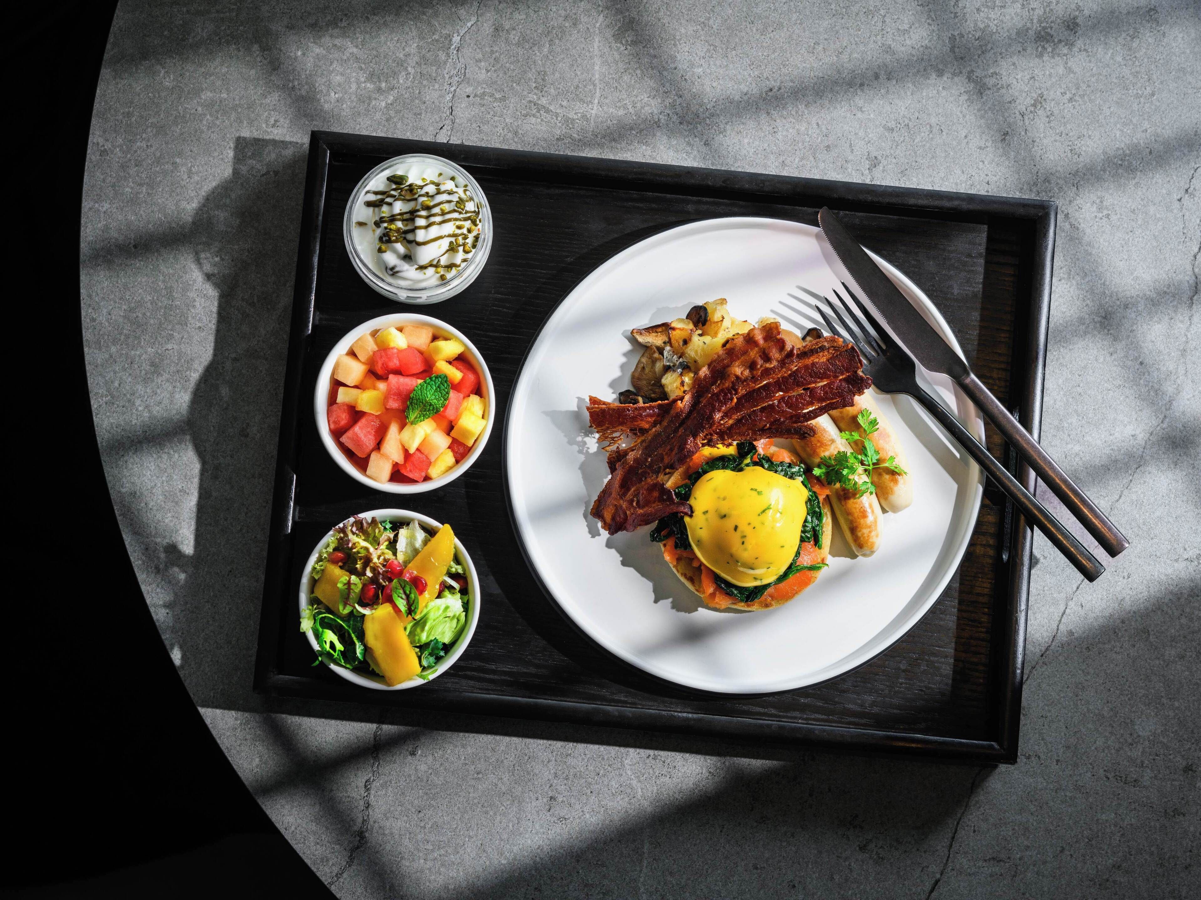 A tray with breakfast items including eggs, bacon, toast, fruit salad, and a green salad.