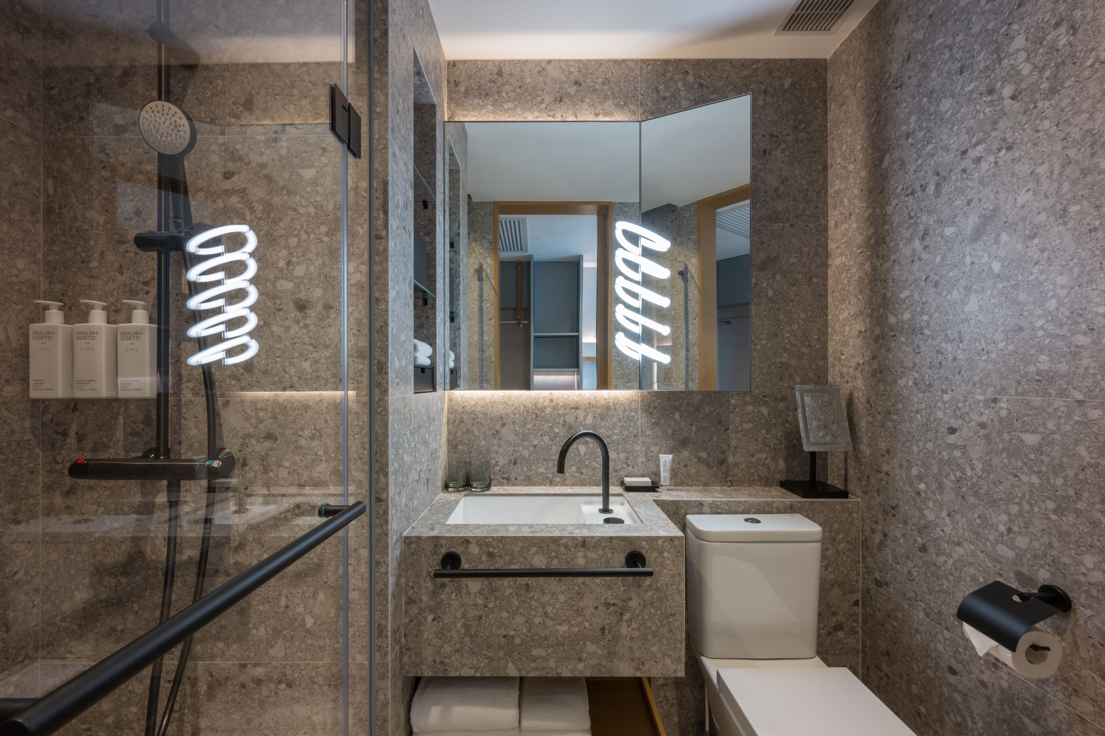 Un baño moderno con ducha de vidrio, lavamanos con espejo y retrete.