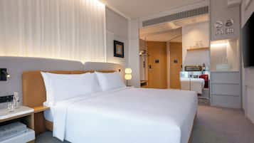 A modern hotel room with a large bed, bedside tables, a TV, and a walk-in closet.