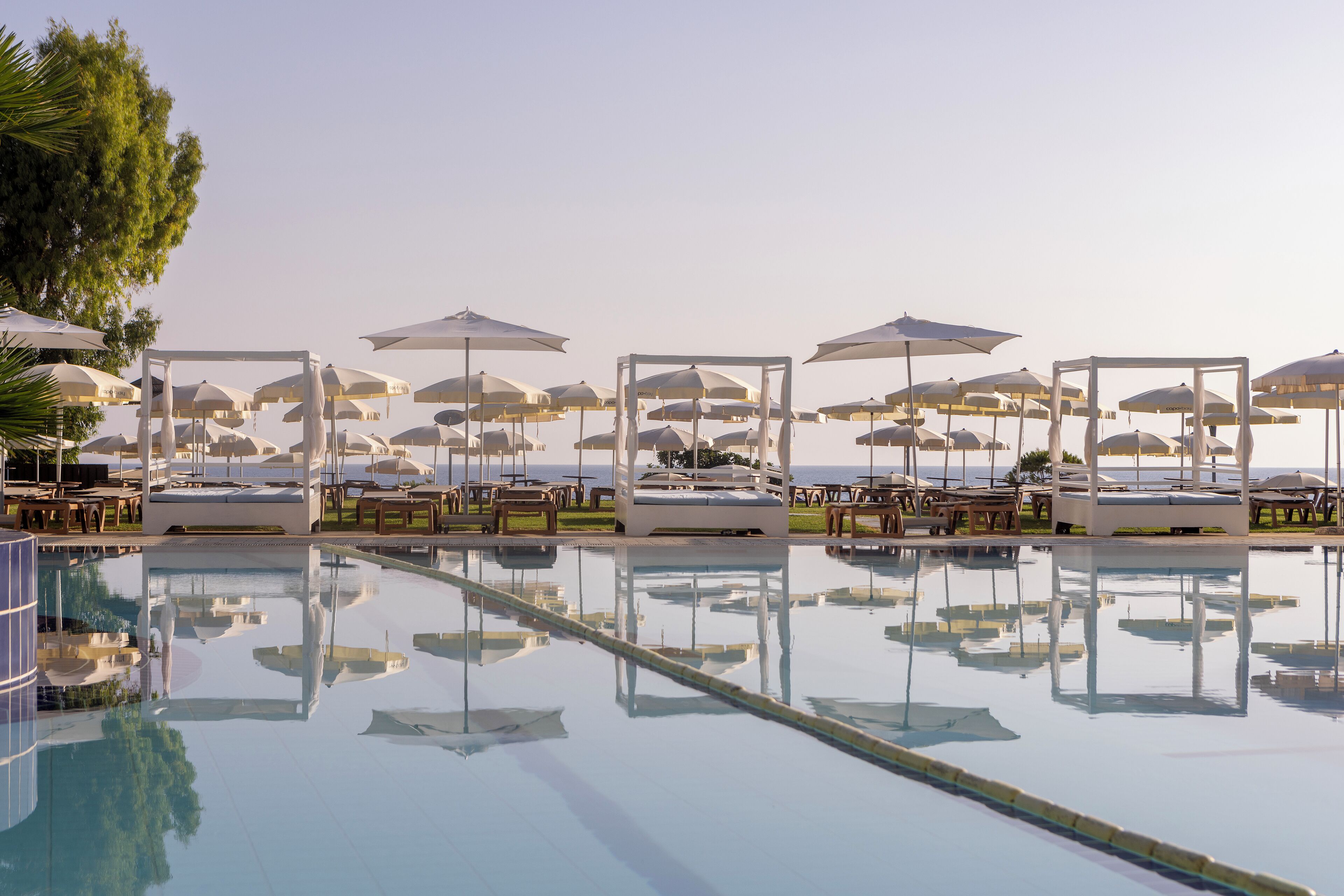 Zona de piscina con sillones y sombrillas, que refleja el paisaje circundante.