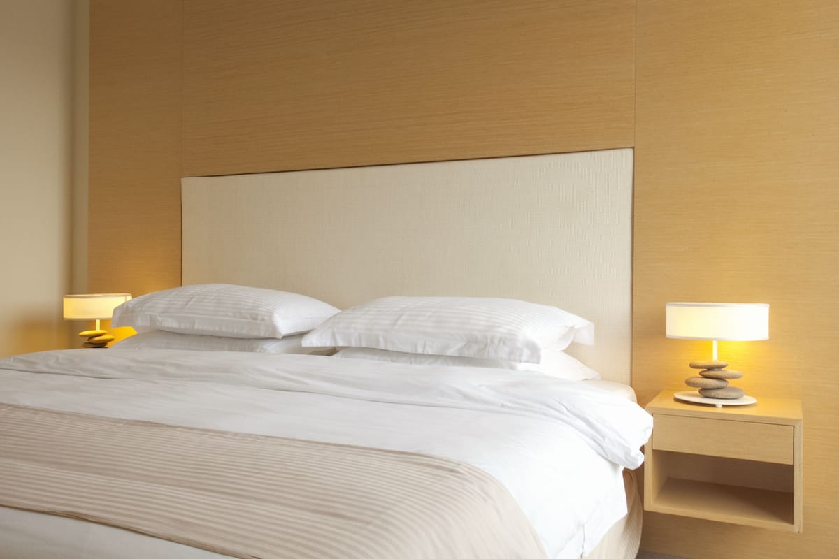 A neatly made bed with white linens and pillows, a wooden headboard, and two bedside tables with lamps.