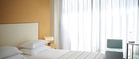 A hotel room with two beds, a nightstand with a lamp, a chair, and a small table with a bottle and a bowl.