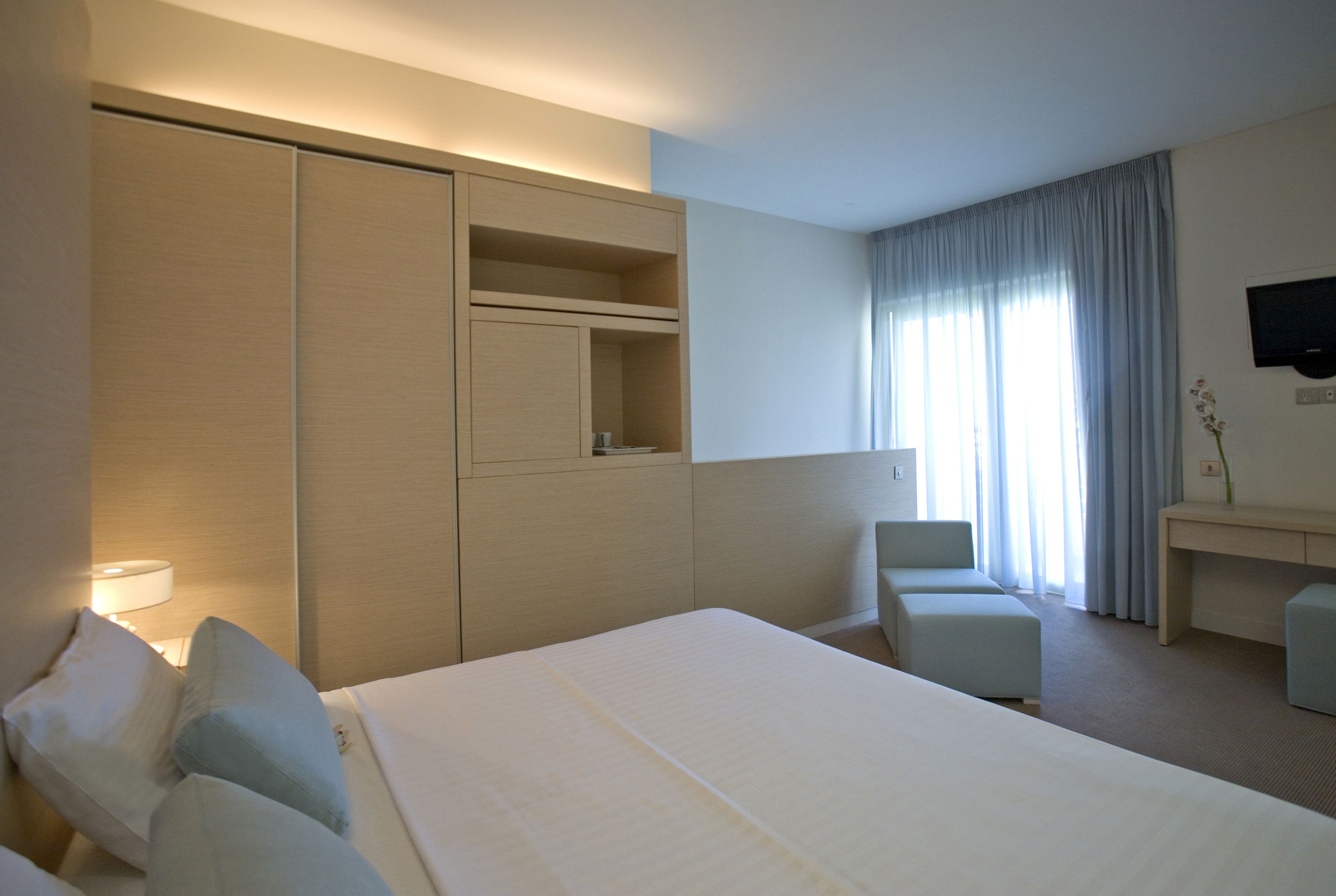 A hotel room with a large bed, a desk, a chair, and a TV mounted on the wall.
