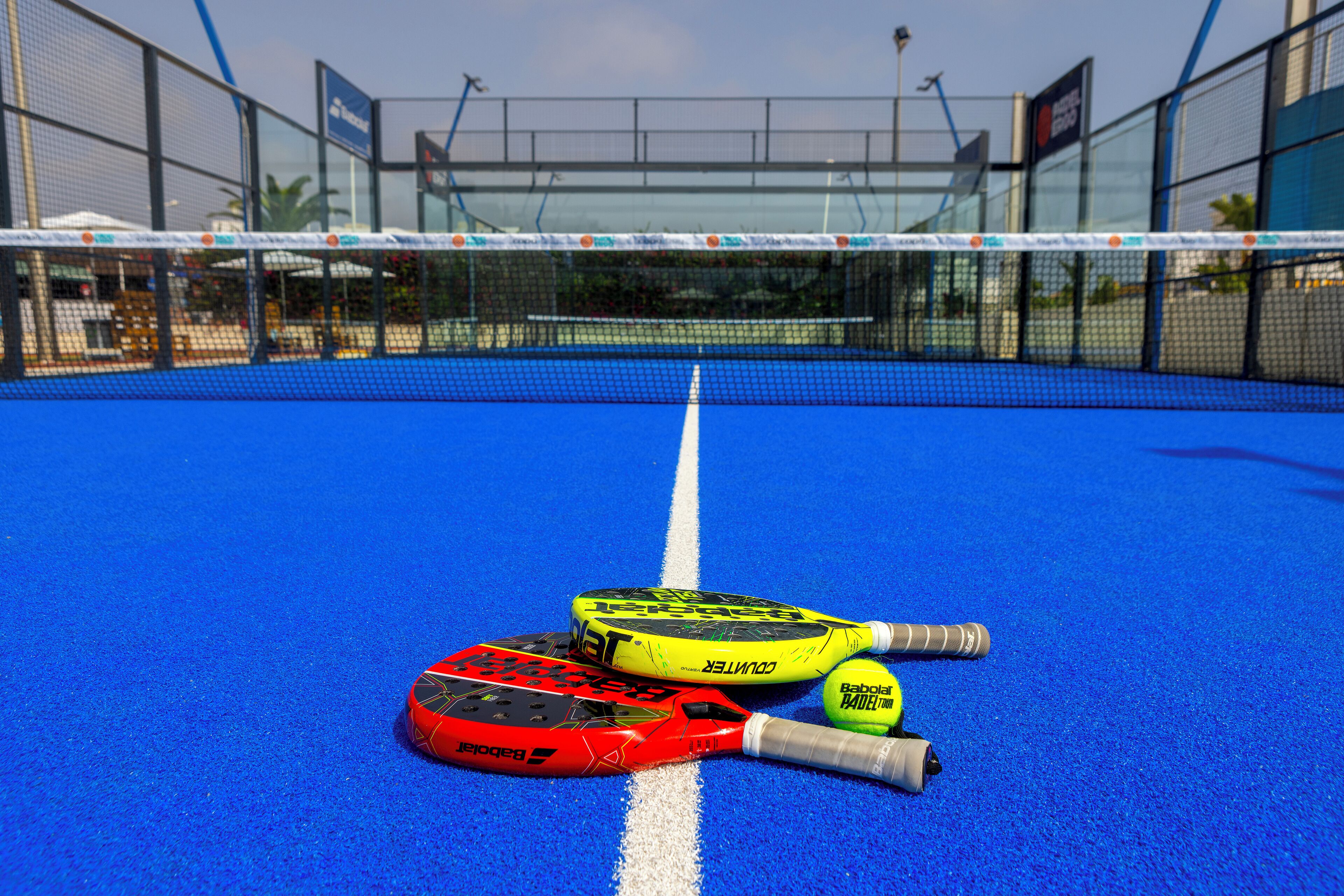 Een blauwe tennisbaan met een net, twee tennisrackets en een tennisbal.