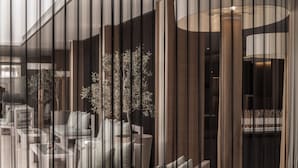 A modern interior with a seating area, a potted plant, and a large window with vertical blinds. - Capo Bay Hotel (Paralimni)