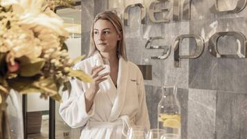 A person in a white robe standing in a spa area with a large floral arrangement and a glass of water.
