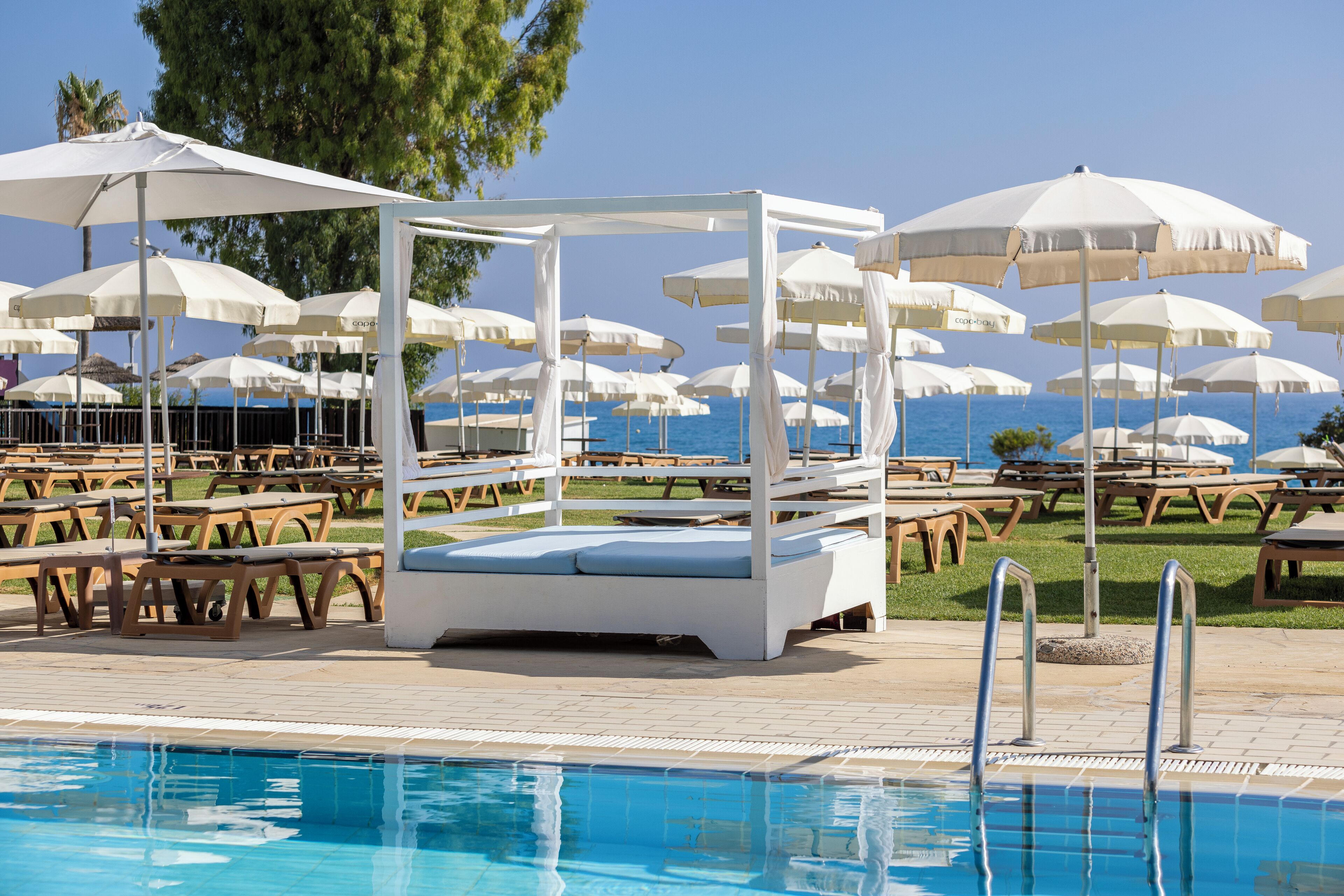 A poolside area with white canopies, lounge chairs, and a clear view of the sea.