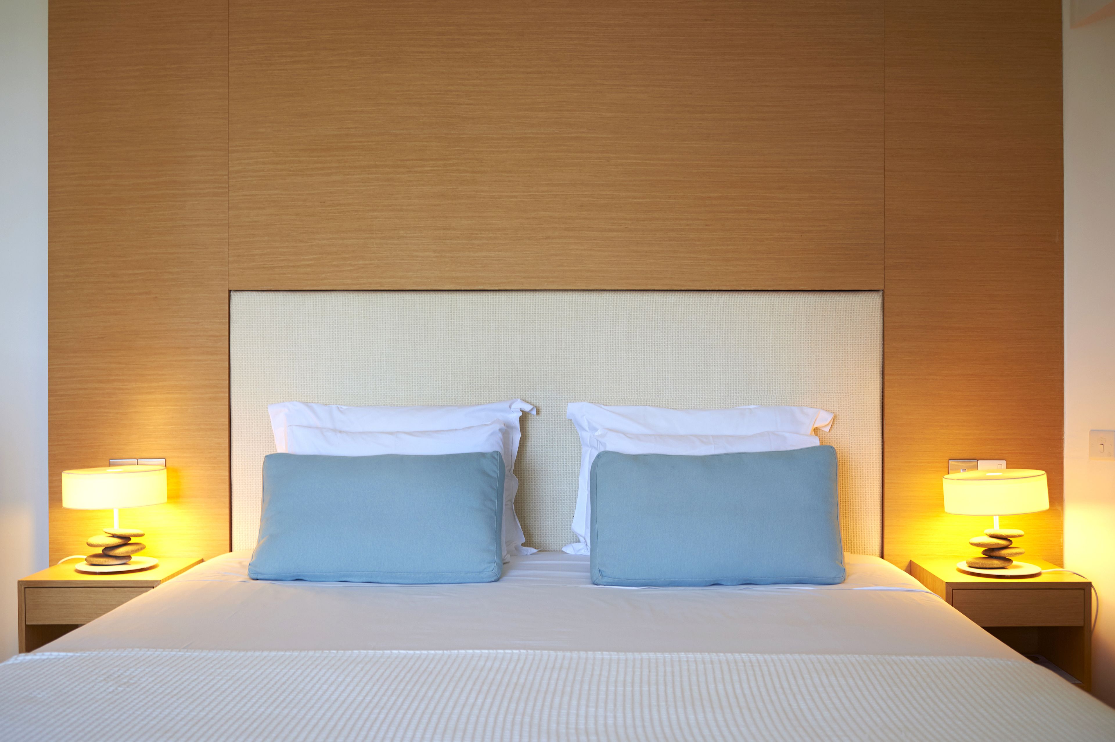 Ein Hotelzimmer mit einem großen Bett, zwei Kissen, einem Nachttisch mit Lampe und einem hölzernen Kopfteil.