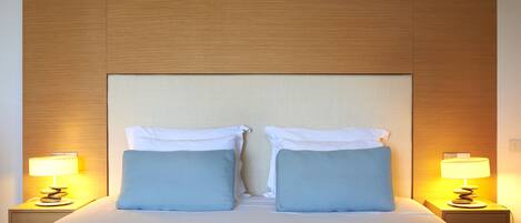 Ein Hotelzimmer mit einem großen Bett, zwei Kissen, einem Nachttisch mit Lampe und einem hölzernen Kopfteil.