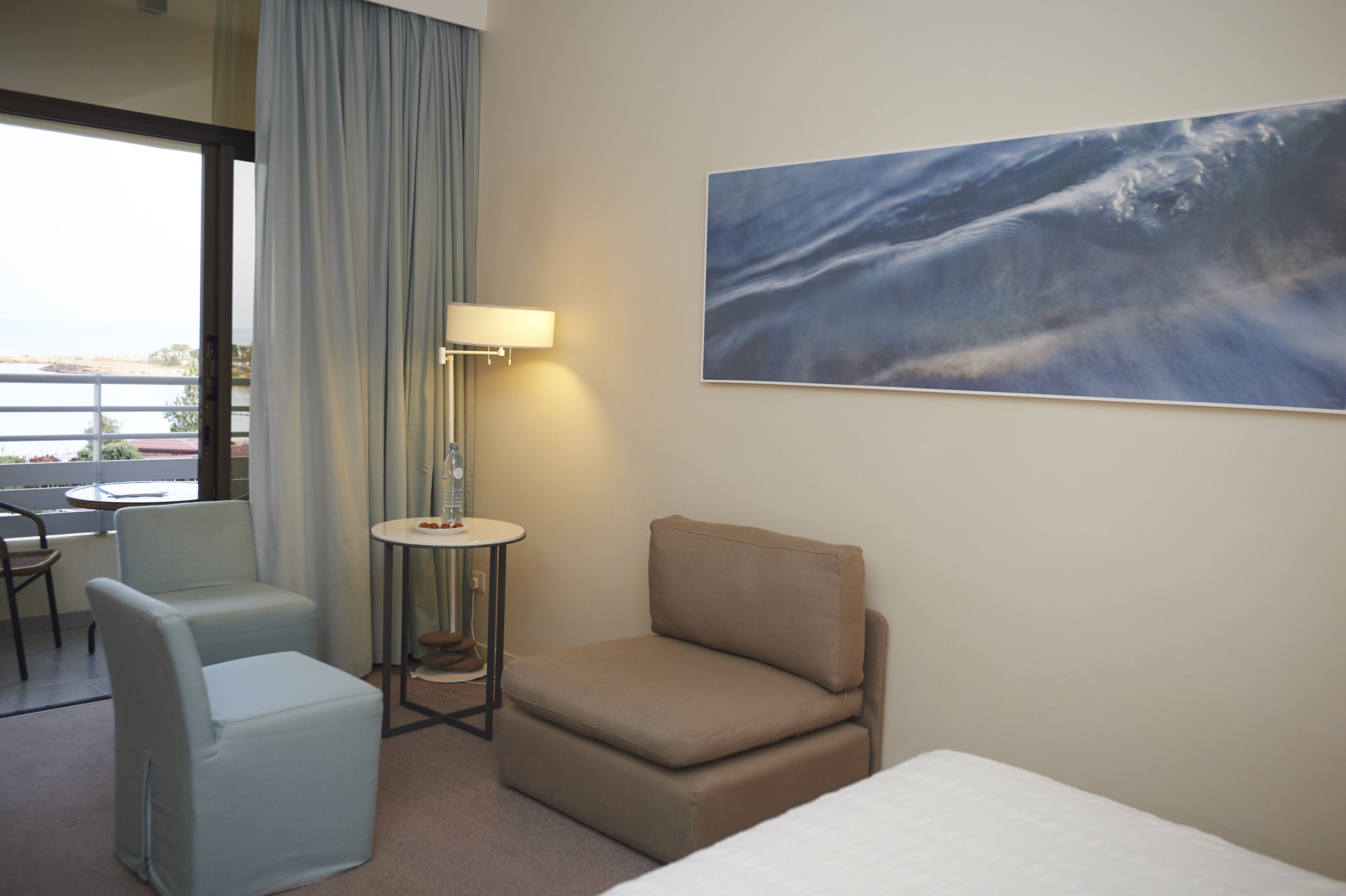Una habitación de hotel con una cama, una mesita pequeña, dos sillas, una lámpara y un cuadro grande en la pared.