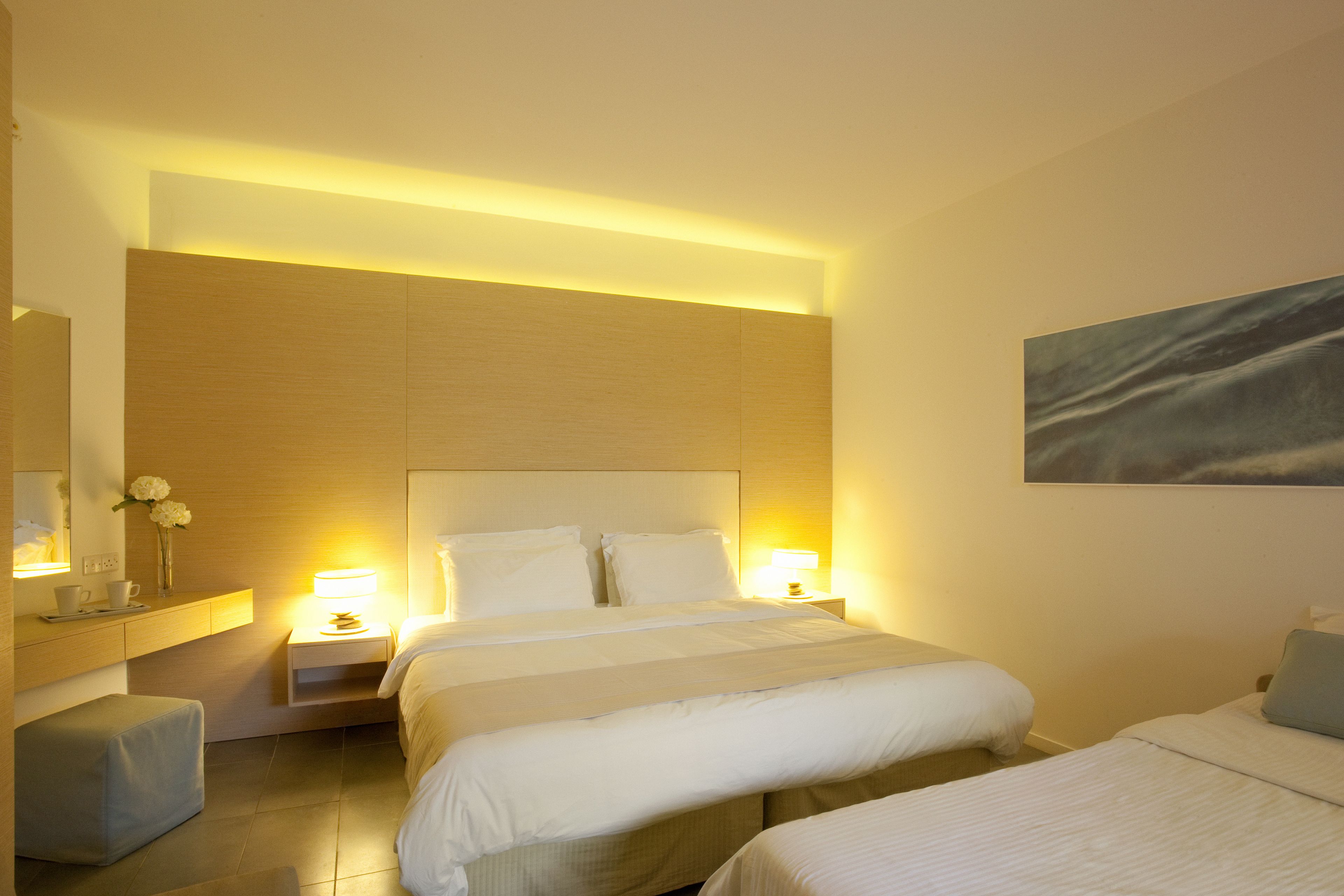 A hotel room with a large bed, bedside tables with lamps, a small seating area, and a painting on the wall.