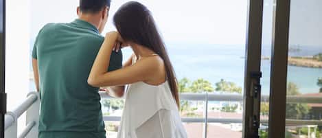 A couple standing by a window overlooking a scenic view of the ocean and a distant shoreline.