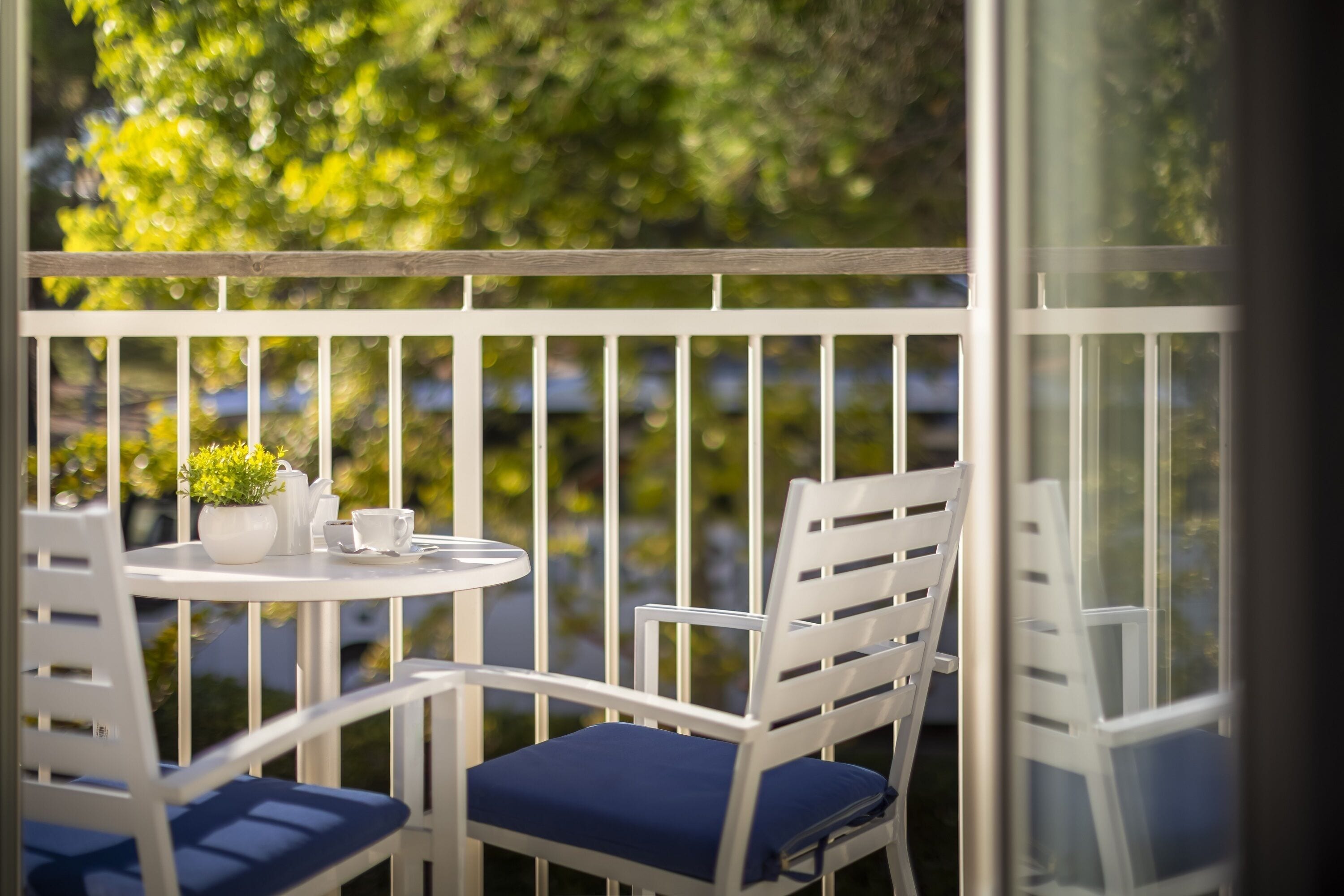A balcony with white railings, a round table, two white chairs with blue cushions, and a potted plant.