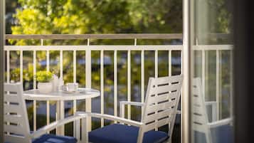 A balcony with white railings, a round table, two white chairs with blue cushions, and a potted plant.