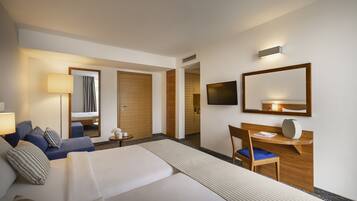 A hotel room with a bed, a desk, a chair, a TV, and a mirror.