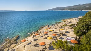 A beach with umbrellas and lounge chairs, a rocky shoreline, and a clear view of the sea and distant hills.