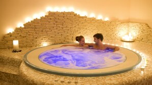 A couple in a circular hot tub with mosaic tile flooring and a brick wall backdrop.