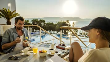 Un comedor con vista a la piscina, una mesa con productos para el desayuno y un libro.
