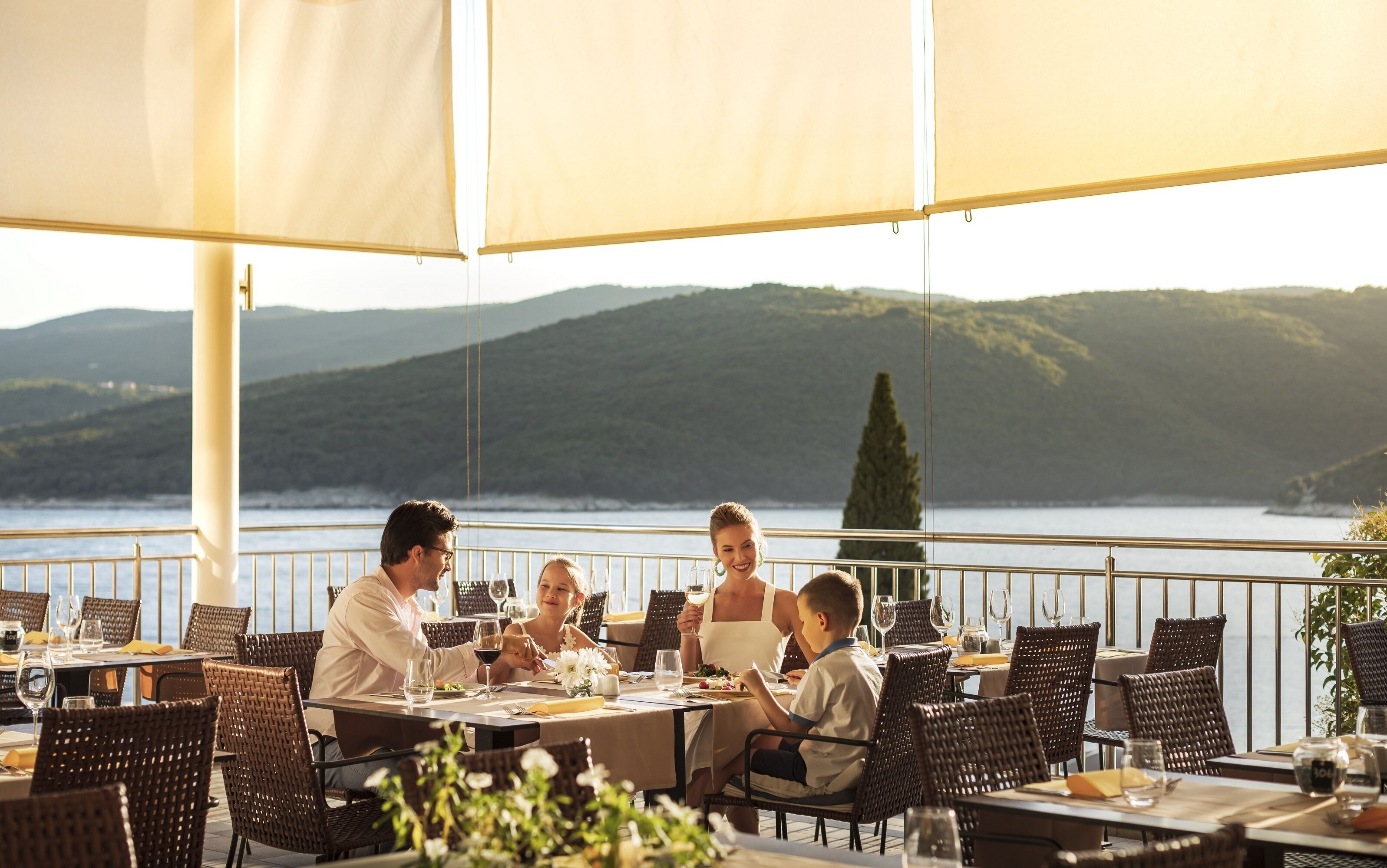 A dining area with tables and chairs, overlooking a body of water and hills.