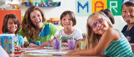 A classroom with children engaged in a craft activity, featuring educational materials and a colorful alphabet display on the wall.