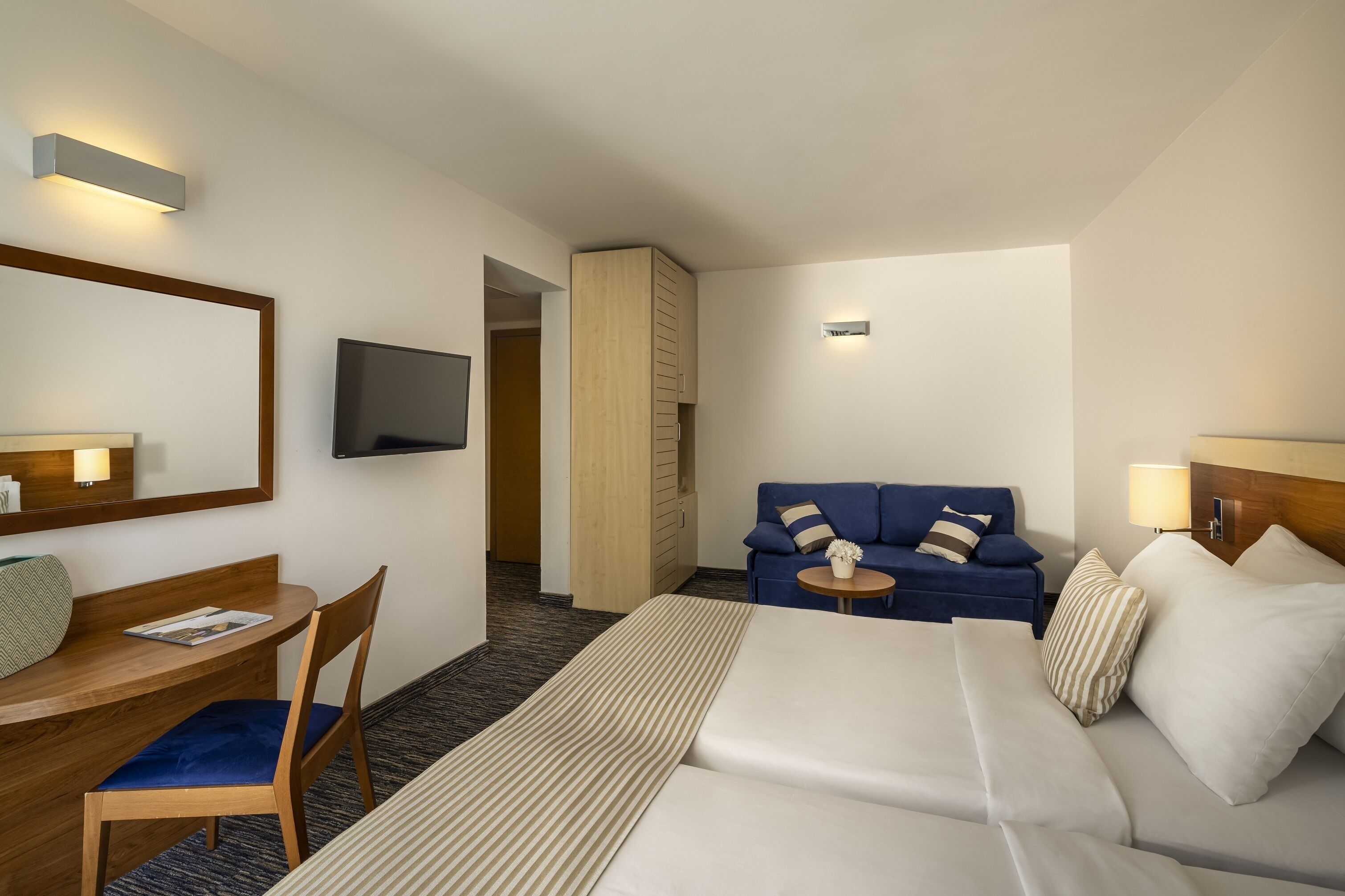 A hotel room with a bed, a desk, a chair, a sofa, and a TV.
