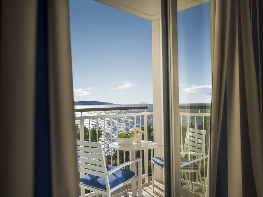 A balcony with white chairs and a small table with a bowl of fruit and flowers.