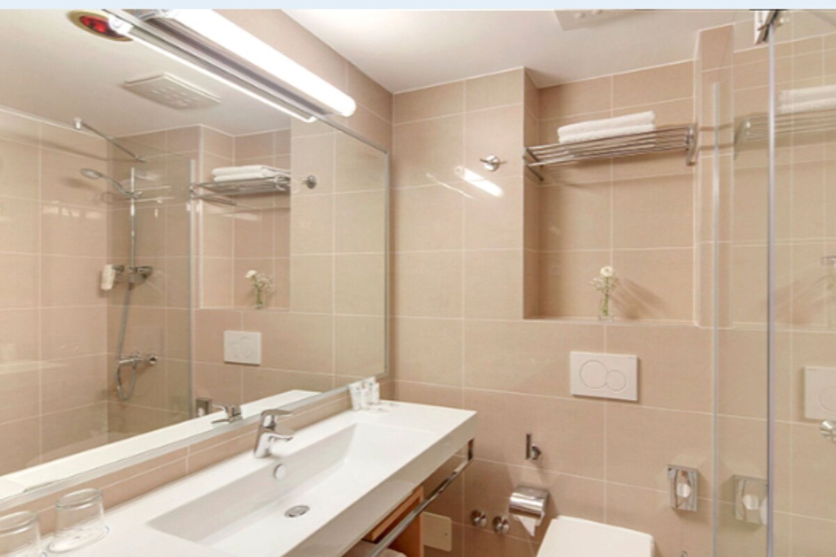 A modern bathroom with a glass shower enclosure, a large mirror, and a white sink.