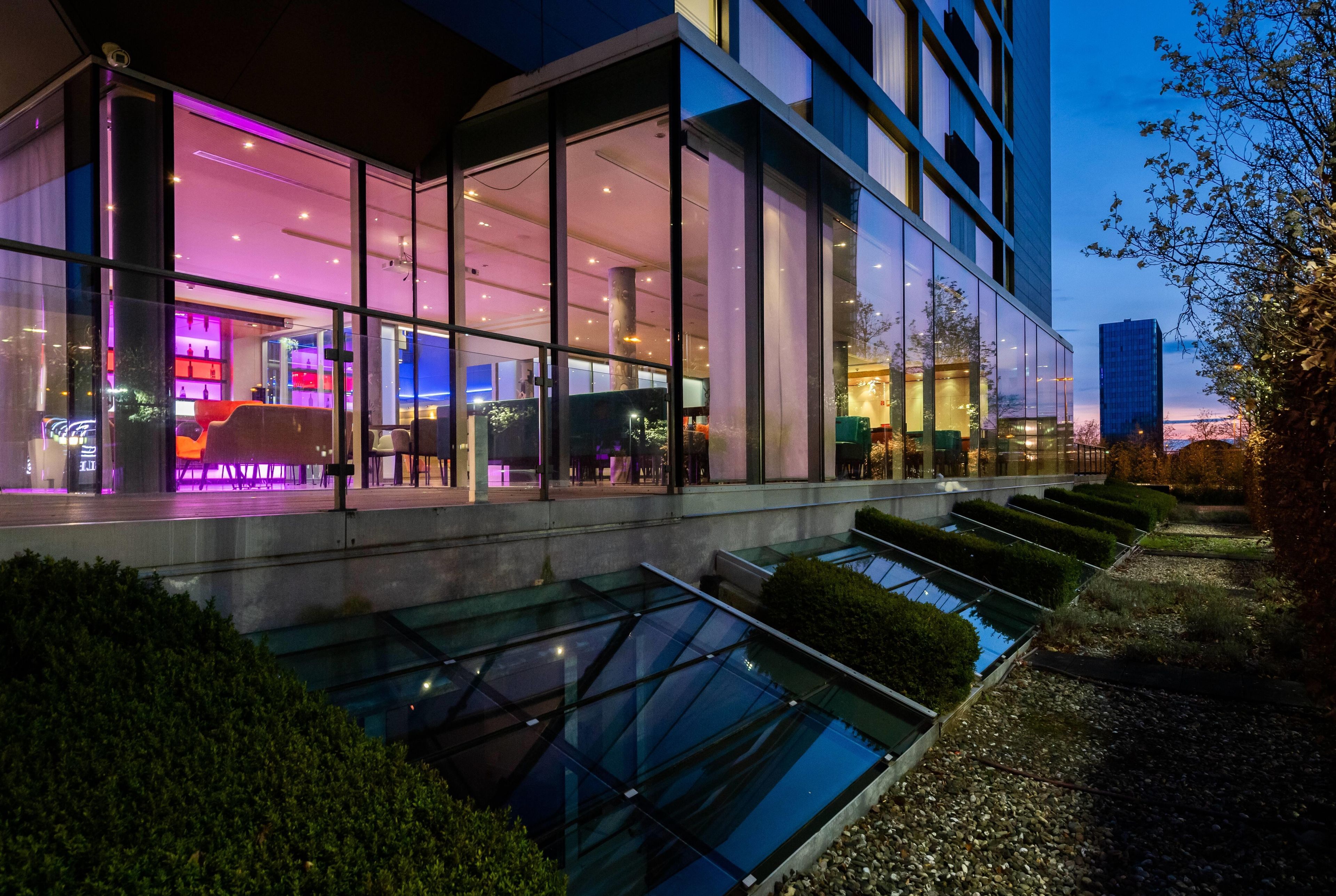 Un edificio moderno con amplios ventanales, un jardín en la azotea y una piscina reflectante.