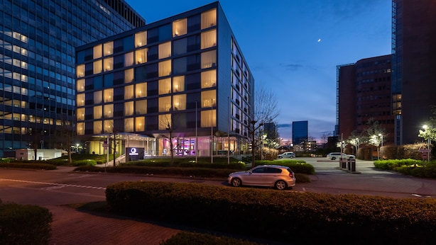 Un hotel moderno con fachada de vidrio, varios pisos y una entrada bien iluminada.