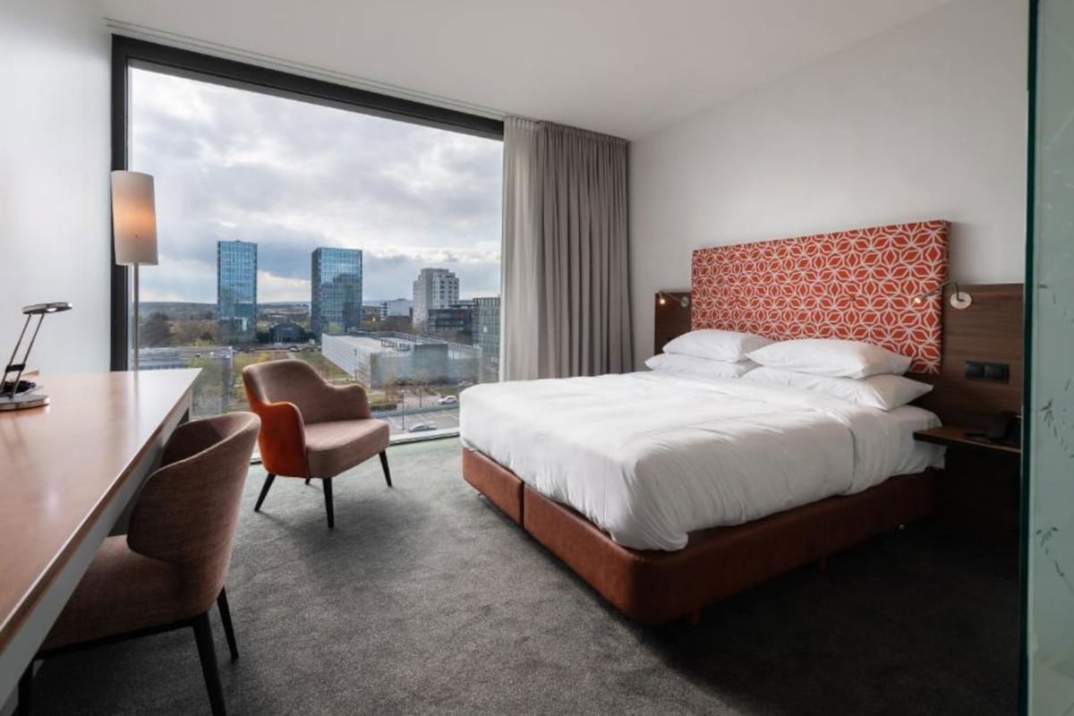 Habitación de hotel con una cama grande, un escritorio, dos sillas, vista a la ciudad y un cabecero estampado.
