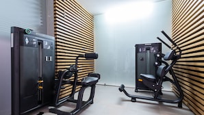 Un gimnasio con dos máquinas de ejercicio, una para extensión de espalda y otra para extensión de piernas, frente a una pared con listones de madera.