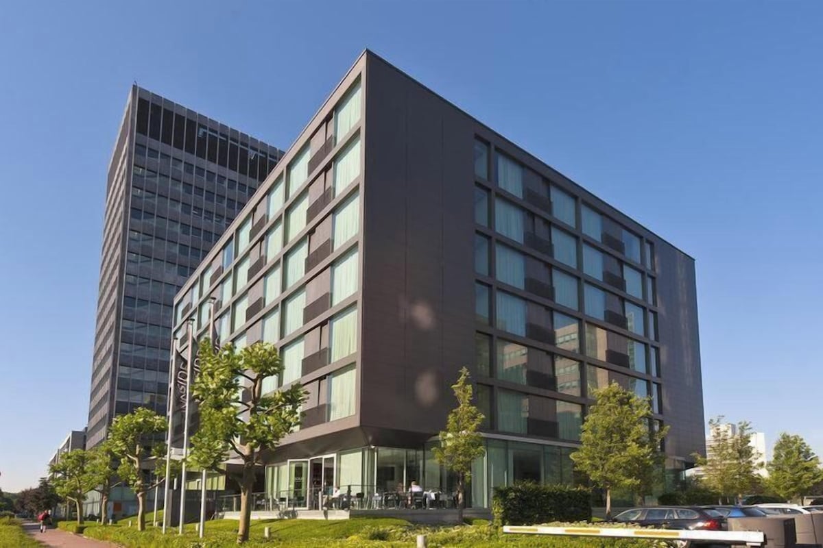 Un edificio moderno con fachada de vidrio, techo plano y un área de estacionamiento con automóviles.