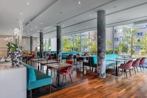Ein modernes Restaurant mit Holzböden, Sitzgelegenheiten in Türkis und Rot und großen Fenstern mit Blick auf die Stadt.