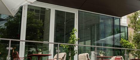 An outdoor seating area with tables and chairs, a large umbrella, and a glass building facade.