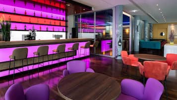 Eine Bar mit einer leuchtenden Neonreklame über einer Flaschenauslage, einer Theke mit Telefon und Registrierkasse sowie Sitzgelegenheiten mit runden Tischen und Stühlen.