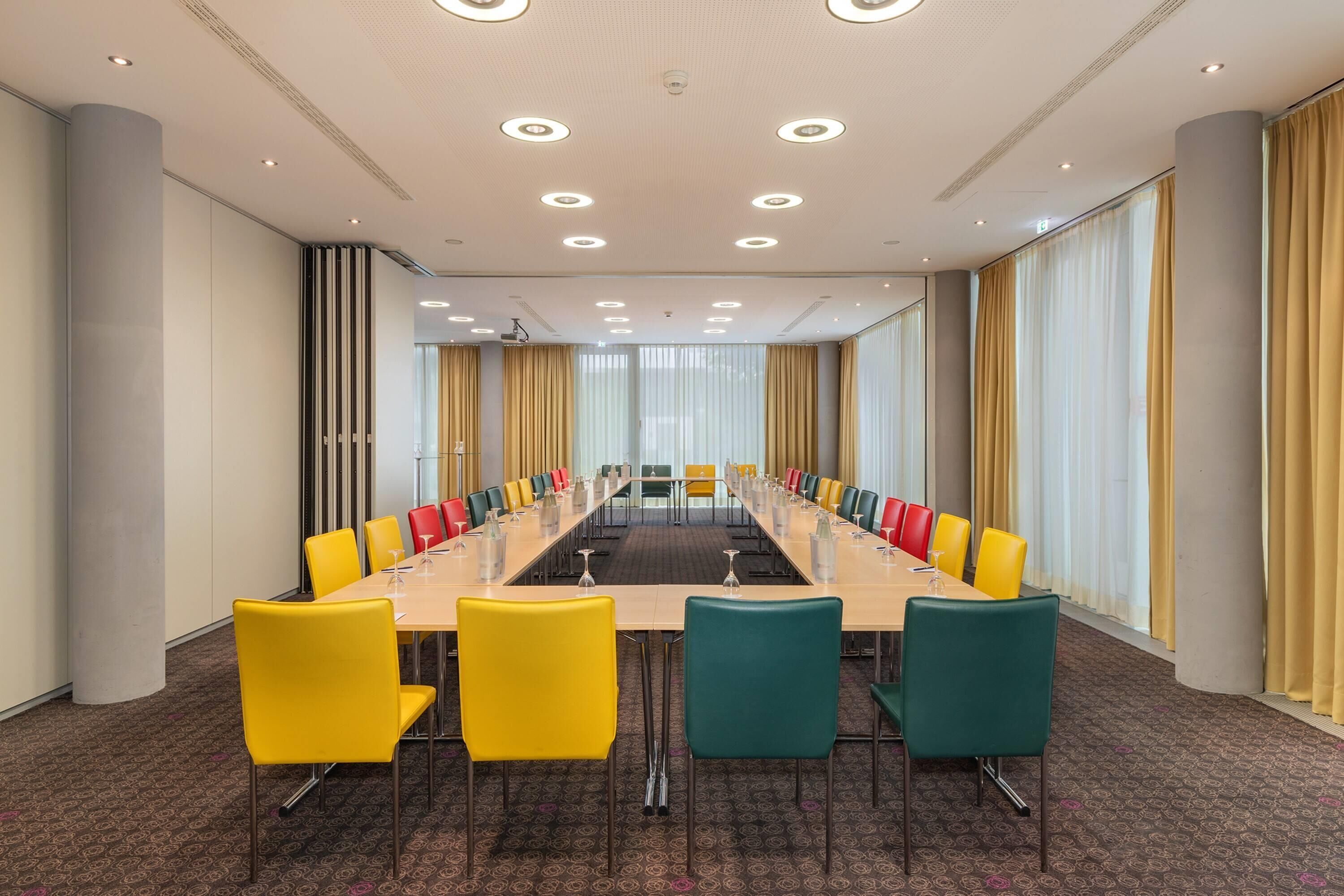 Uma sala de conferências com uma mesa comprida, várias cadeiras e grandes janelas com cortinas.