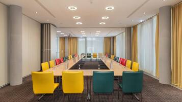 Uma sala de conferências com uma mesa comprida, várias cadeiras e grandes janelas com cortinas.