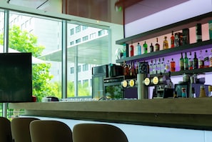 Zona de bar con estantes llenos de botellas de licores, una máquina de café y un televisor.