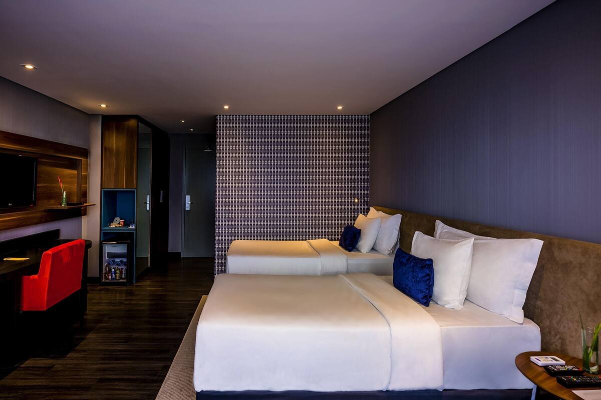 Ein modernes Hotelzimmer mit Schlafsofa, Fernseher, Minibar und einer Wand mit Muster.