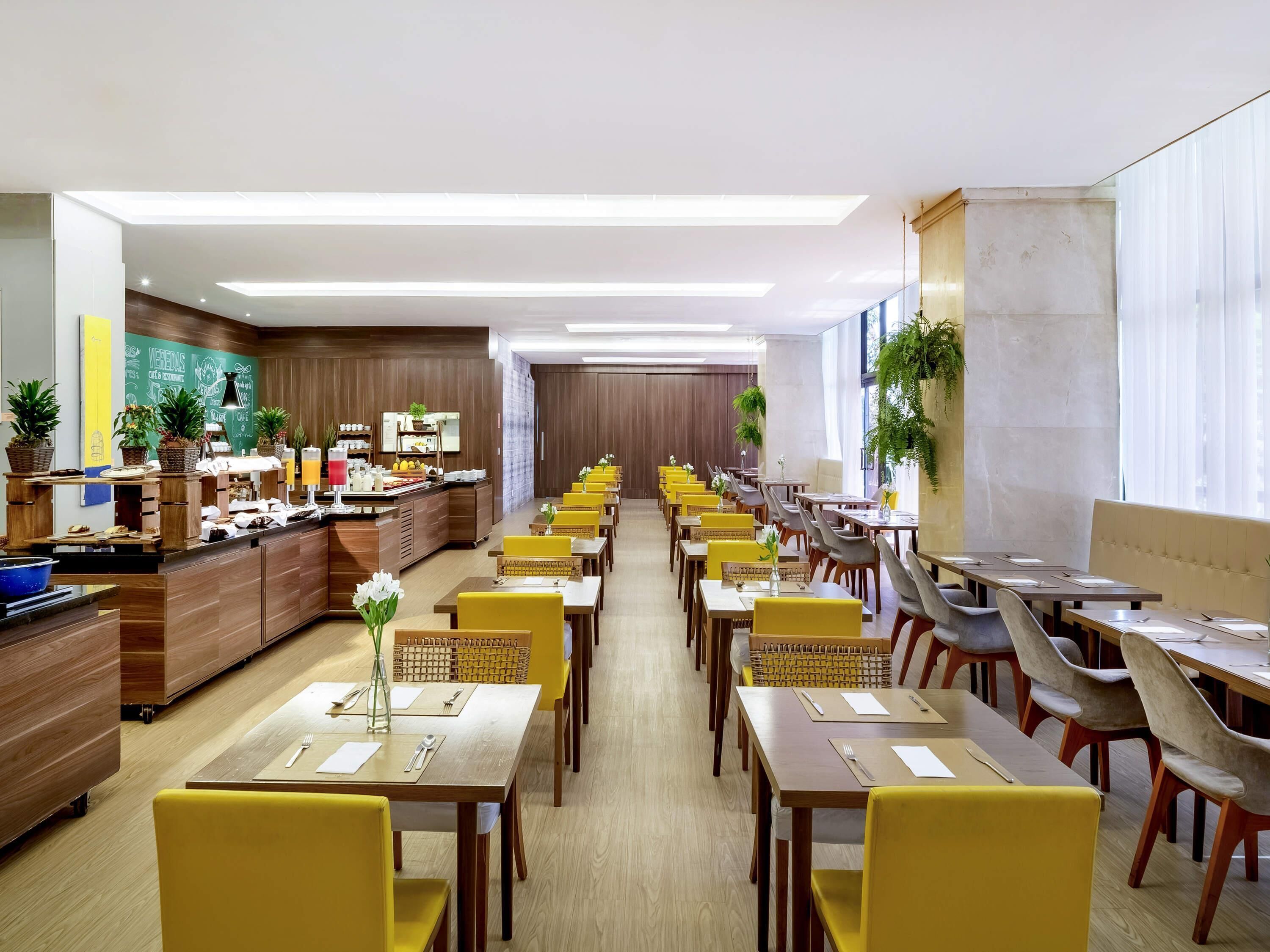 A spacious restaurant with multiple dining tables and chairs, a buffet area, and large windows providing natural light.
