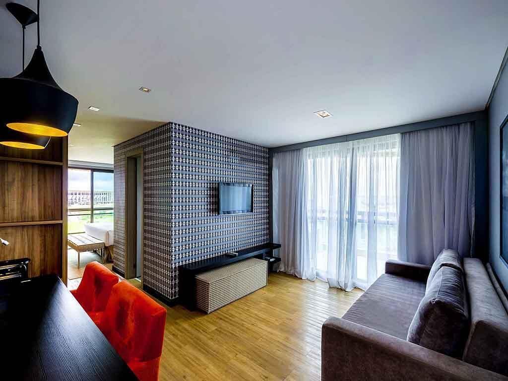 Un salon moderne avec un téléviseur, un plancher en bois, un canapé, un fauteuil rouge et une suspension noire.