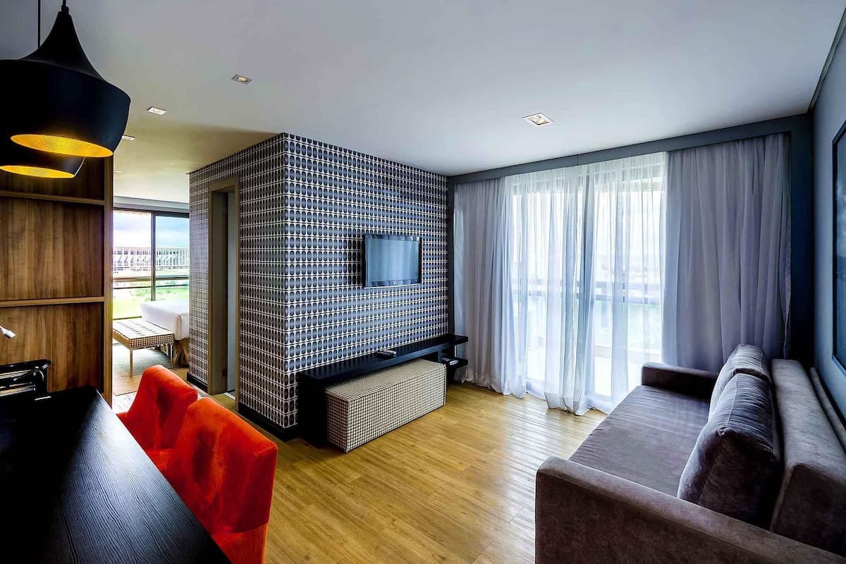 Ein modernes Wohnzimmer mit an einer strukturierten Wand montiertem Fernseher, Holzboden und einem großen Fenster mit Vorhängen.