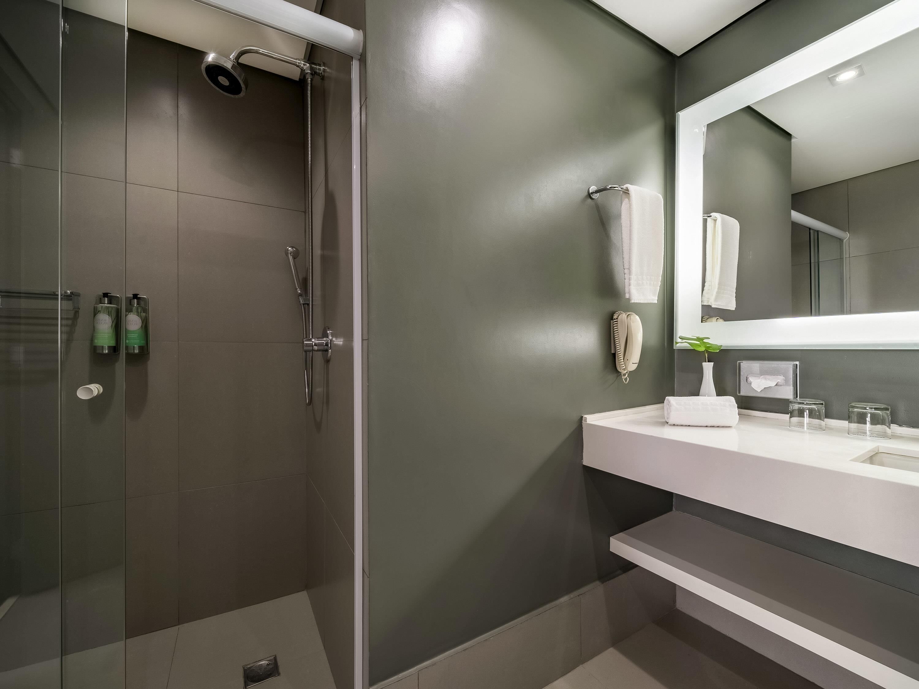 A modern bathroom with a glass-enclosed shower, a white vanity with a mirror, and a green wall.
