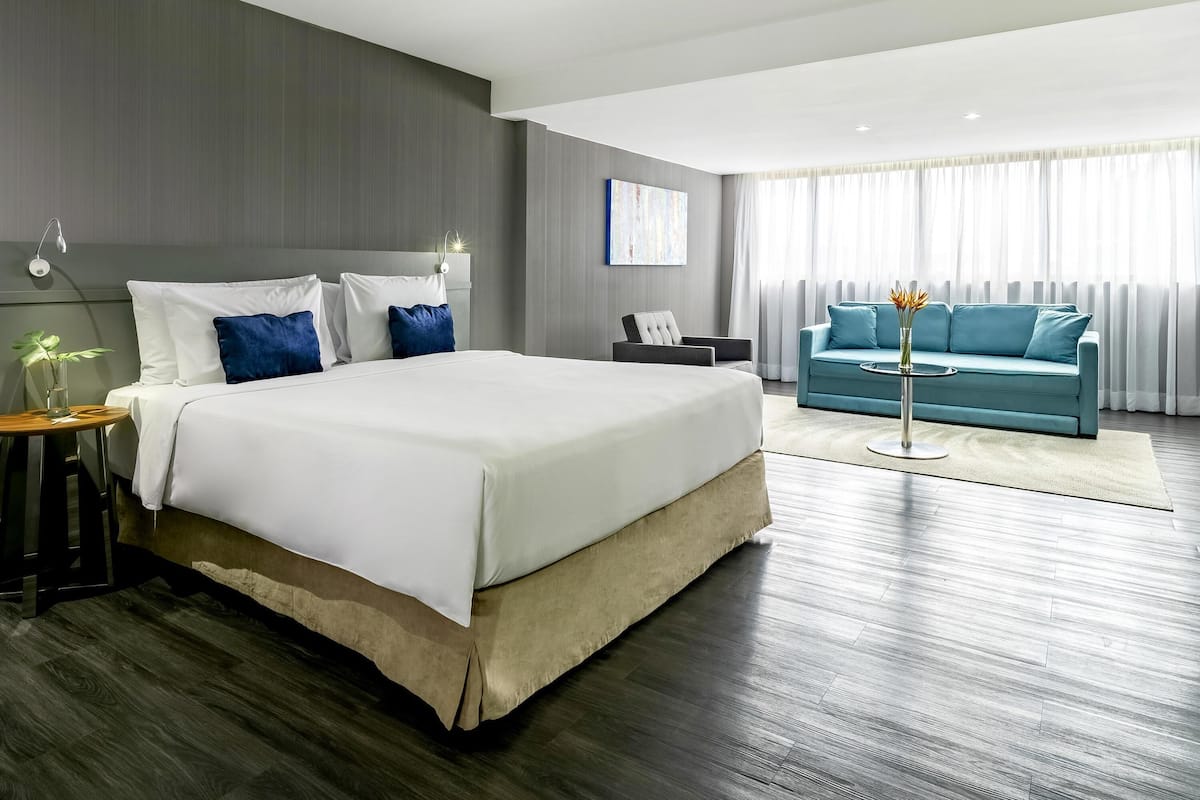Ein modernes Hotelzimmer mit einem großen Bett, einer Couch, einem kleinen Tisch und einer Lampe.