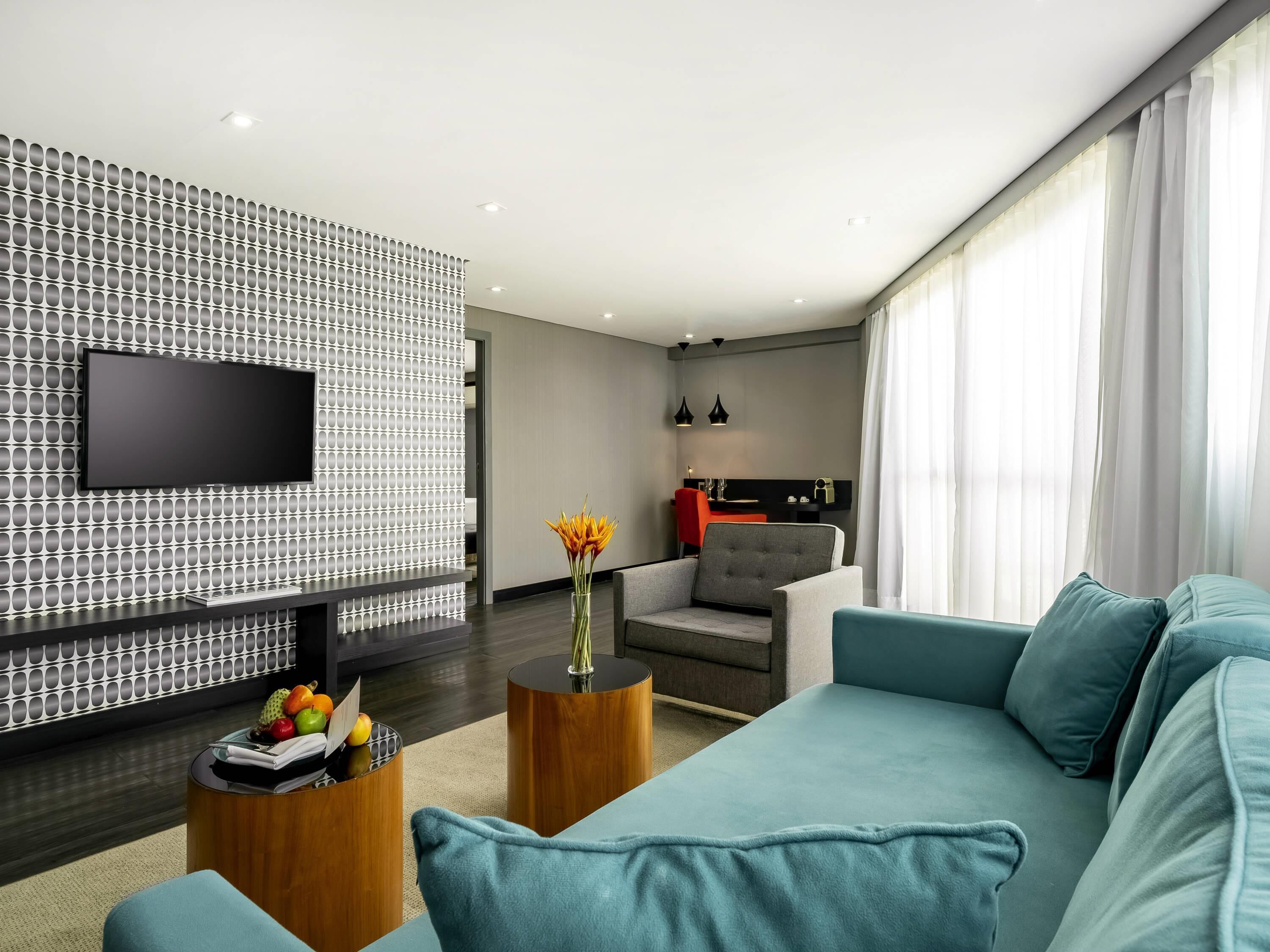 Ein modernes Wohnzimmer mit Flachbildfernseher, einer Couch, einem Couchtisch mit Obst und einem Essbereich mit einem roten Stuhl.