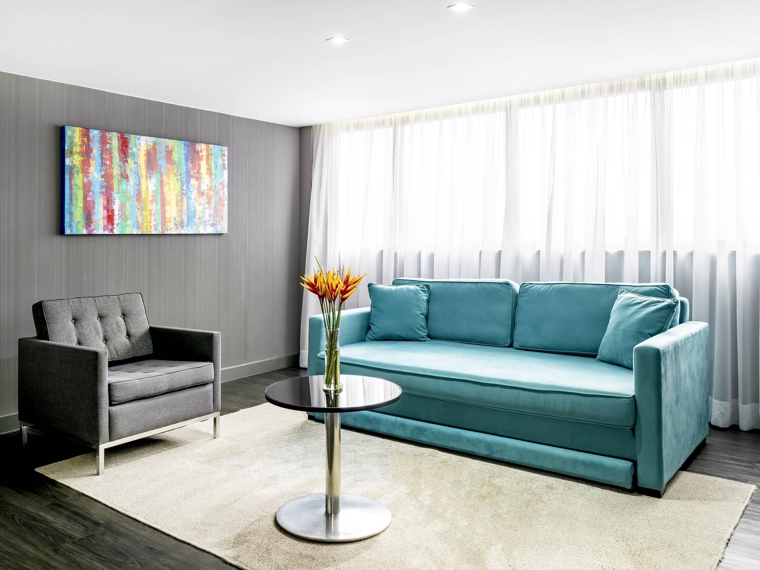 Uma sala de estar moderna com um sofá cinzento, uma poltrona cinza, uma mesa de centro redonda e um quadro abstrato colorido na parede.
