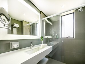 Un baño moderno con un espejo grande, un lavabo, una ducha y una ventana.
